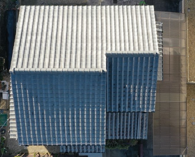 施工前の屋根を真上から撮影した写真。全体に瓦が敷かれており、経年劣化による色褪せやムラが見られる。寄棟構造の二階建て住宅の屋根形状がよくわかる構図。