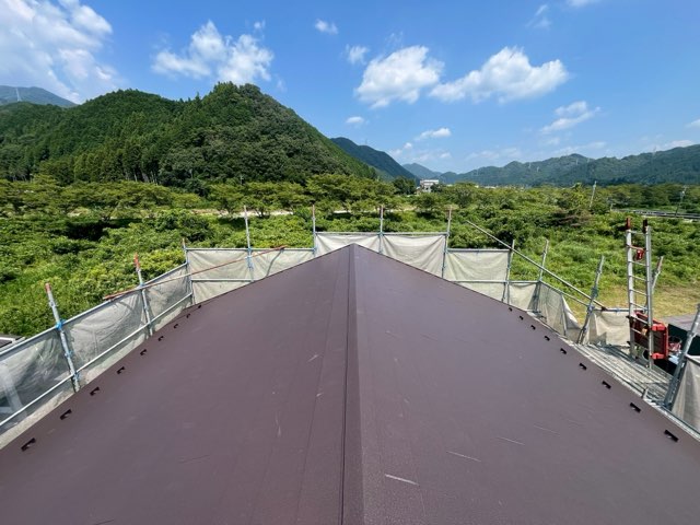 施工完了後の屋根全景。スーパーガルテクト（シェイドブラウン）が美しく敷かれ、青空と山並みに映える。