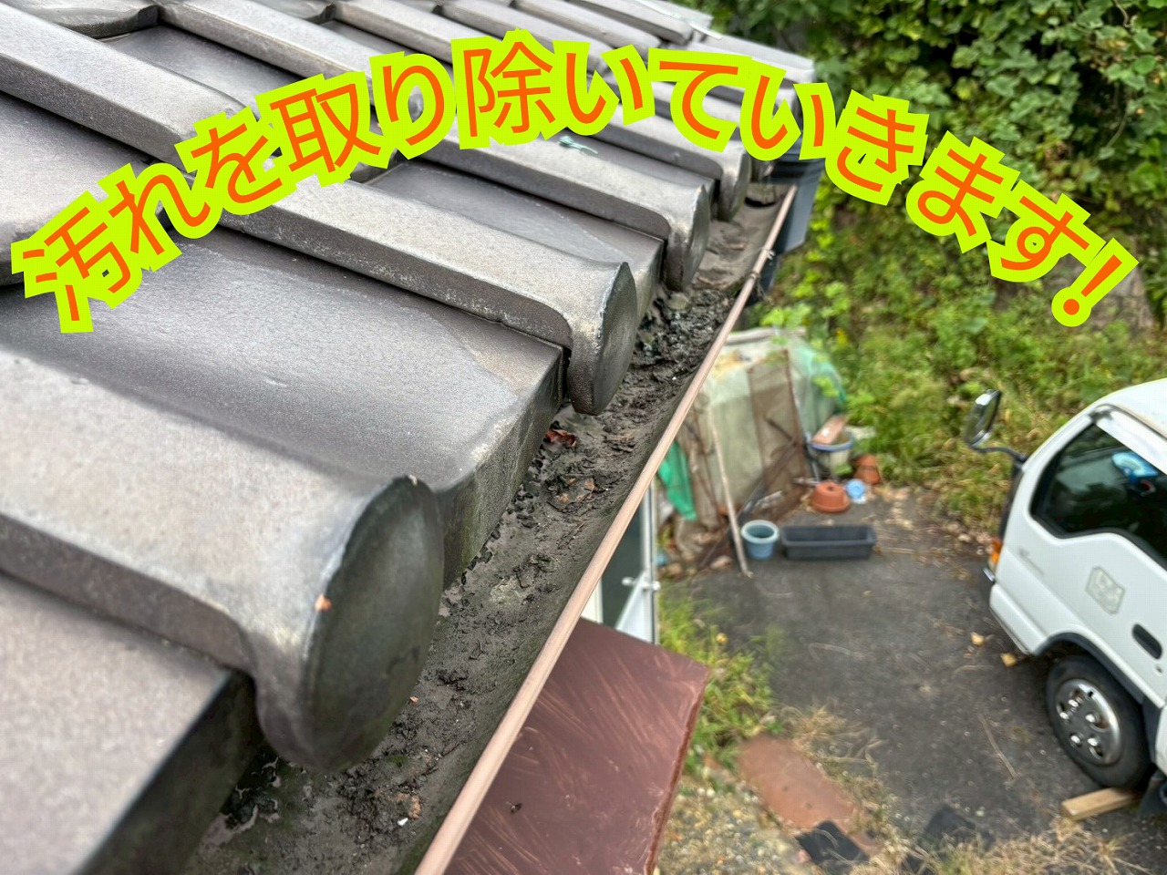 屋根の上から職人が雨樋の汚れを取り除いている様子