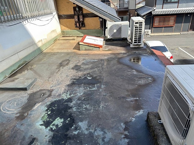 屋上防水が劣化し、防水層の剥がれや色ムラ、水たまりが発生している施工前の屋上の様子