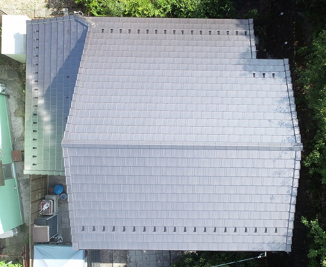 多治見市小名田町にて屋根の葺き替え工事が完了した後のドローン撮影写真。屋根全体が均一に施工され、棟部分や屋根材の納まりもきれいに整った仕上がりの様子が確認できる。