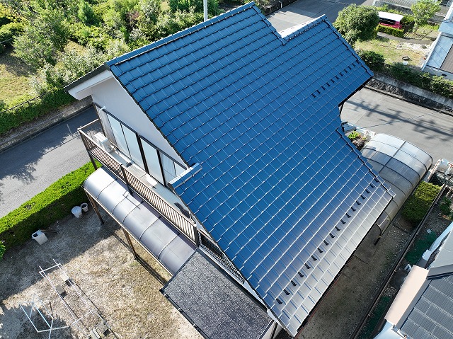 多治見市小名田町にて屋根の葺き替え工事と雨樋交換工事が完了した住宅の全景。ドローンで撮影した青色屋根材の美しい仕上がりが確認できる施工後の写真。