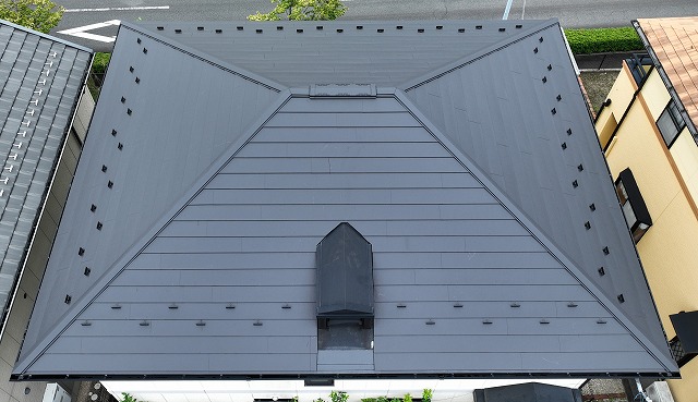 可児市みずきヶ丘で施工完了後の屋根をドローンで撮影。IG工業スーパーガルテクト（シェイドブラック）が美しく輝き、落ち着いた高級感のある仕上がりになっている様子。
